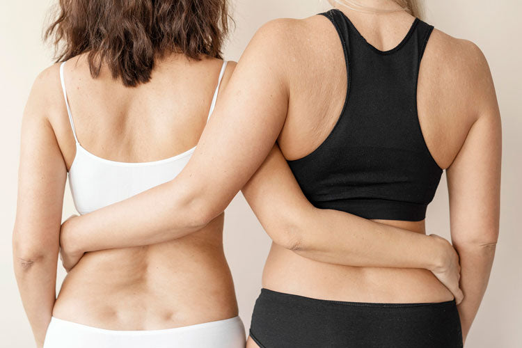 draudzenes, kam uzvilkta koriģējošā un bezvīļu apakšveļa, stāv ar mugurām pret kameru